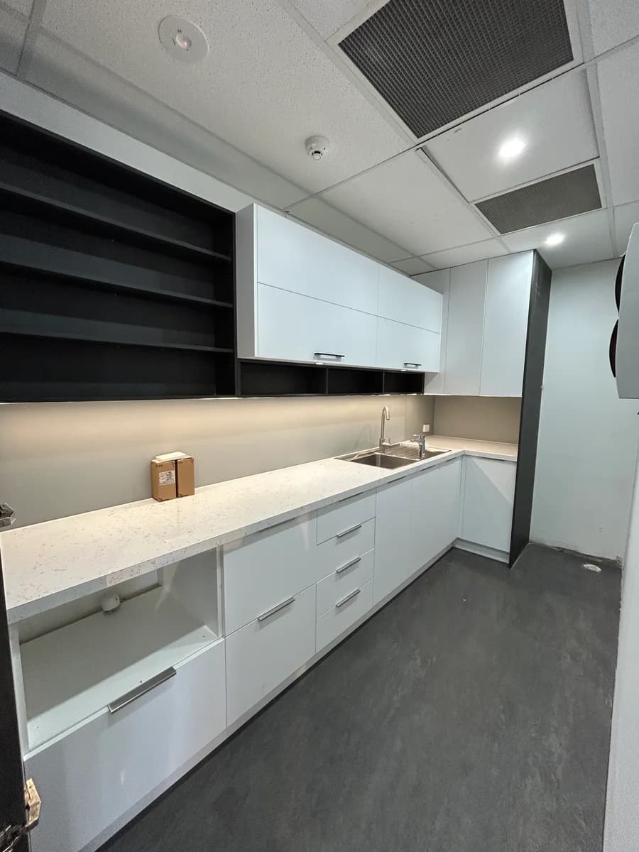 Finished commercial kitchenette with white cabinetry and dark shelving